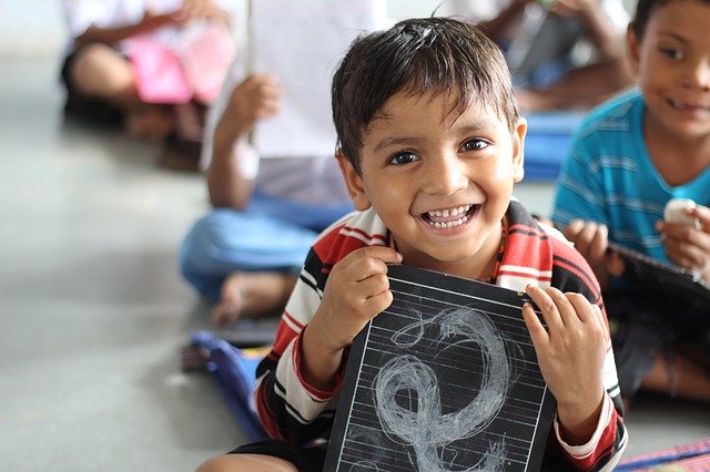 A young latino child smiles as he presents a drawing on a chalk board slate.