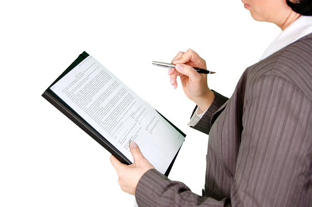 A female in a grey business suit looks over her paperwork while holding a silver pen in her right hand.